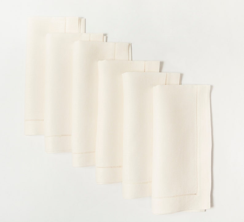 Puede incluir: Seis servilletas de tela color crema dispuestas en diagonal. Cada servilleta doblada presenta un borde decorativo cosido a lo largo de un borde. Las servilletas est&aacute;n hechas de una tela lisa de color s&oacute;lido.