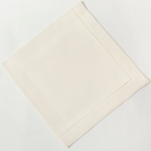 Puede incluir: Servilleta cuadrada de color marfil con un borde cosido. La servilleta est&aacute; hecha de una tela tejida y se muestra sobre un fondo blanco. Los detalles de costura a&ntilde;aden un toque de elegancia al dise&ntilde;o sencillo.