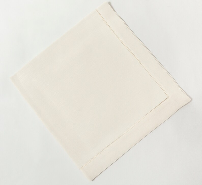 Puede incluir: Servilleta cuadrada de color marfil con un borde cosido. La servilleta est&aacute; hecha de una tela tejida y se muestra sobre un fondo blanco. Los detalles de costura a&ntilde;aden un toque de elegancia al dise&ntilde;o sencillo.