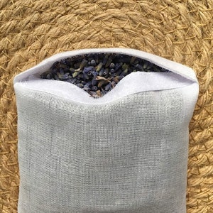 May include: A white mesh pouch filled with dried lavender flowers. The pouch is sitting on a woven straw surface.