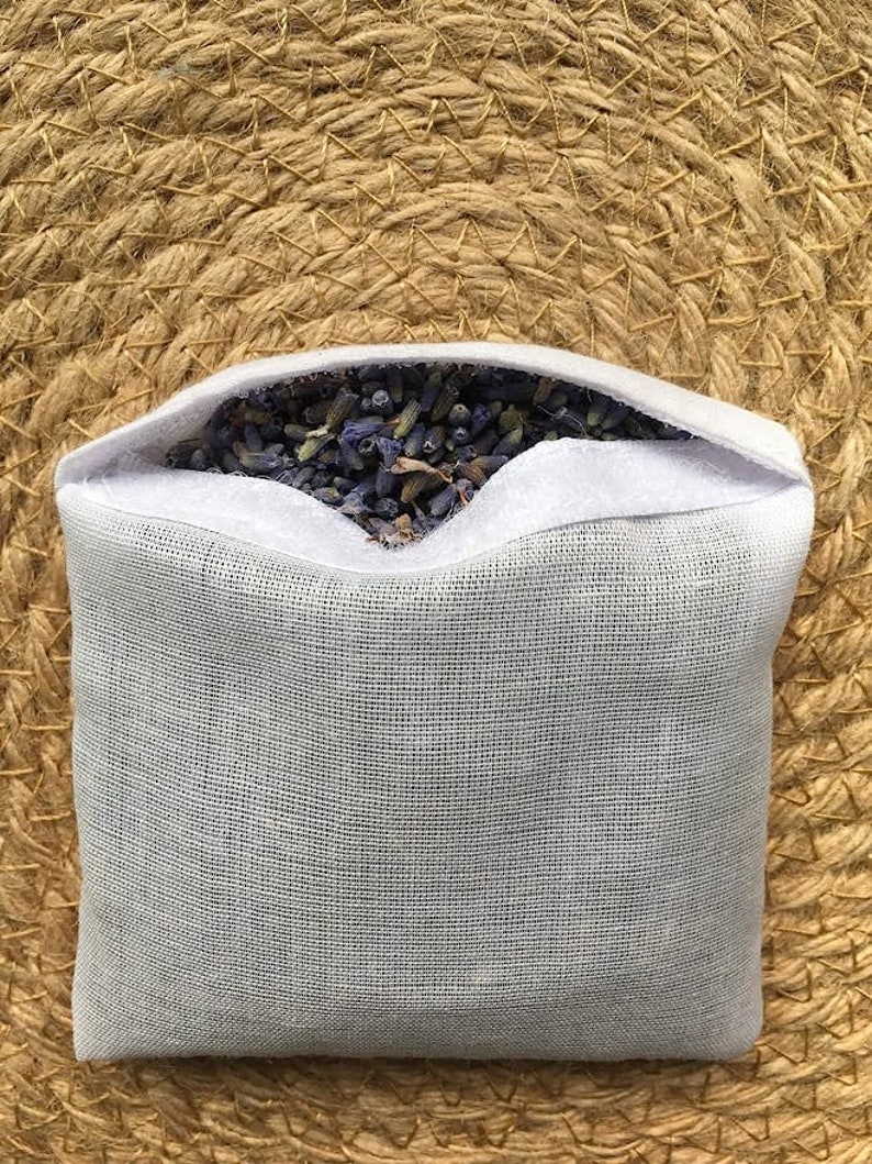May include: A white mesh pouch filled with dried lavender flowers. The pouch is sitting on a woven straw surface.