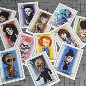 Peut inclure: Un ensemble de cartes à collectionner avec des illustrations de personnages de films d'horreur. Chaque carte a une bordure blanche et un numéro. Les personnages incluent Chucky, Michael Myers et Jason Voorhees, avec du texte.