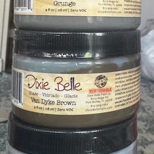 May include: A stack of three 4 fl oz jars of Dixie Belle Glaze. The top jar is Grunge, the middle is Van Dyke Brown, and the bottom is Hi-Ho Silver. Each jar features a black lid, a label with the brand name, color name, and 118 ml volume.