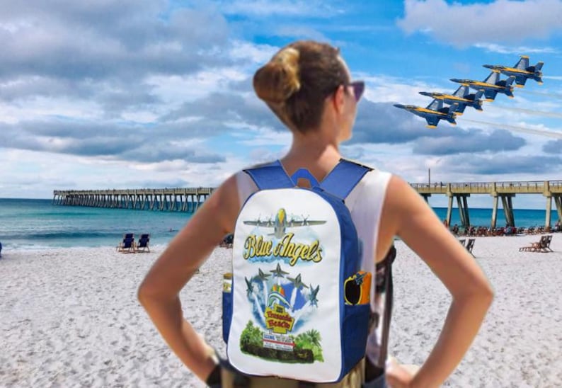 Pu&ograve; includere: Uno zaino blu e bianco con una grafica con la scritta "Blue Angels" e immagini di aerei. Lo zaino &egrave; indossato su una spiaggia con un molo sullo sfondo e le Blue Angels che volano sopra.