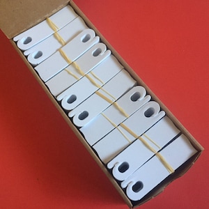May include: A close-up of a box filled with white plastic clips, secured with rubber bands. The clips are arranged in rows and are all the same size and shape.
