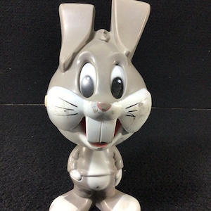 Op de afbeelding: Een grijs plastic Bugs Bunny beeldje met een wit shirt en witte schoenen. Het beeldje heeft een groot hoofd met grote ogen en een brede glimlach.