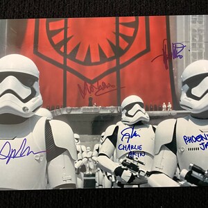 May include: A signed photo of three Stormtroopers from Star Wars: The Force Awakens. The photo is signed by John Boyega, Charlie  and  Phoenix James. The Stormtroopers are standing in front of a red flag with a black symbol.