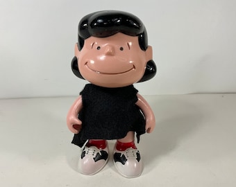 May include: A black and white plastic figurine of a girl with black hair, wearing a black dress and white shoes with black accents.