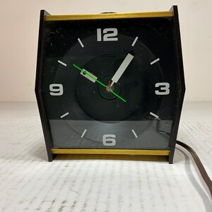 May include: A black and gold alarm clock with a round face and white numbers. The clock has a green second hand and a white minute hand.