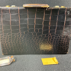 May include: A black leather briefcase with a crocodile pattern. The briefcase has a brass latch and a brown leather handle.