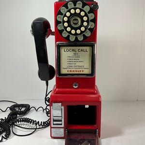 May include: A red Crosley retro payphone with a black handset. The phone has a rotary dial and a coin return slot. The text "LOCAL CALL 10¢" is visible on the front. The phone is a vintage style.