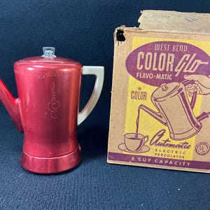 May include: A vintage red electric percolator with a white handle and a clear knob, next to its original box. The box features the text "COLOR GLO FLAVO-MATIC" and an illustration of the percolator. The box is slightly damaged.