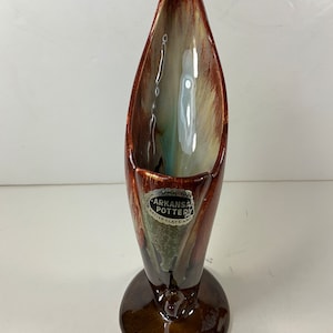 Op de afbeelding: Een bruine en witte geglazuurde keramische vaas met een unieke blaadjesvorm. De vaas heeft een ronde basis en een label met de tekst "Arkansas Pottery from Native Clays and Glazes".
