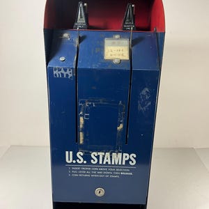 Puede incluir: Una máquina expendedora de sellos estadounidenses vintage azul con una parte superior roja. La máquina tiene dos ranuras para monedas etiquetadas como "Quarter Only" y una palanca para dispensar sellos. La máquina tiene instrucciones que dicen: "Inserte la moneda correcta arriba de su selección. Tire de la palanca hacia abajo hasta el final, luego suelte. La moneda se devuelve cuando se queda sin sellos."