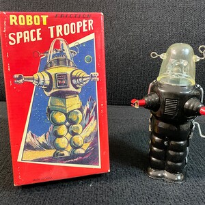 May include: A vintage tin robot toy in black with a clear plastic head. The robot is on a red box with the words "Robot Friction Space Trooper" and "Made in China".