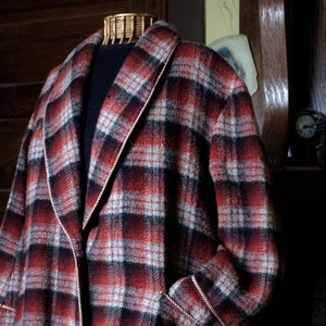 May include: A red, black and white plaid robe with a black collar and a white trim. The robe has a label that reads "Guardsman - Made in New Zealand - clothes".