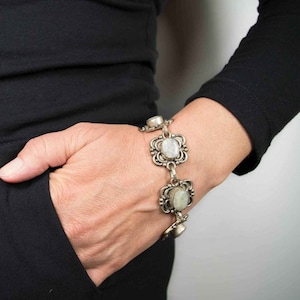 Può includere: Un braccialetto d'argento con pietre ovali bianche incastonate in cornici d'argento ornate. Il braccialetto ha un design a maglie di catena.