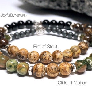 May include: Two beaded bracelets, one with brown and green jasper beads and the other with brown jasper beads. The bracelets are labeled "Pint of Stout" and "Cliffs of Moher".