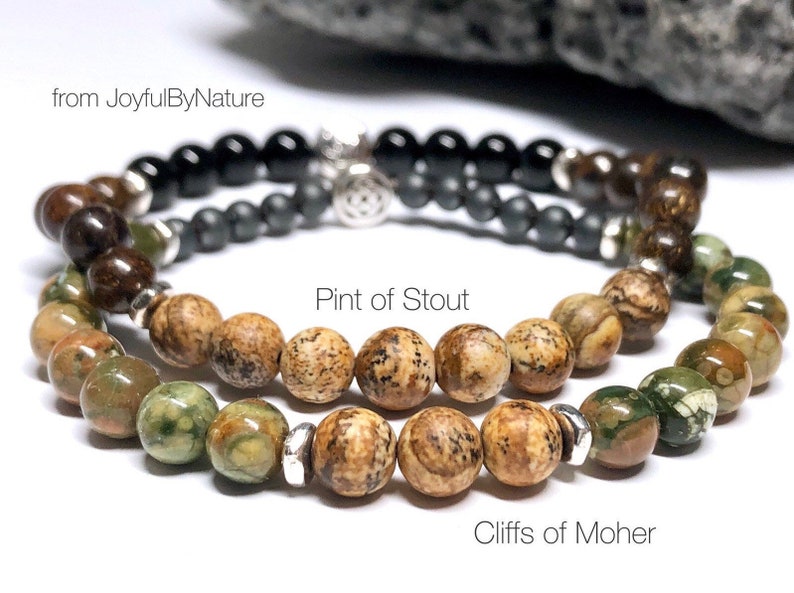 May include: Two beaded bracelets, one with brown and green jasper beads and the other with brown jasper beads. The bracelets are labeled "Pint of Stout" and "Cliffs of Moher".
