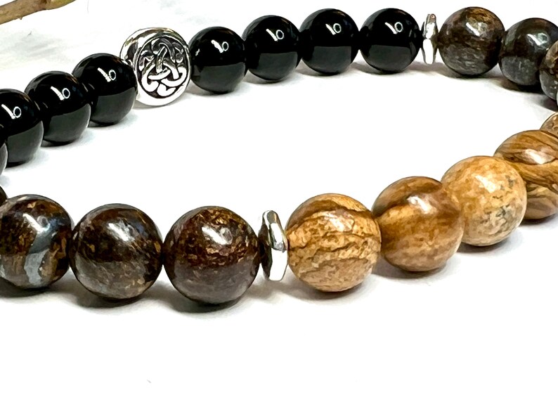 May include: A beaded bracelet with black and brown beads, a silver Celtic knot charm, and a silver spacer bead.