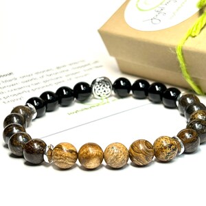May include: A brown and black beaded bracelet with a silver charm. The bracelet has a Celtic knot design charm and is made with natural stones.