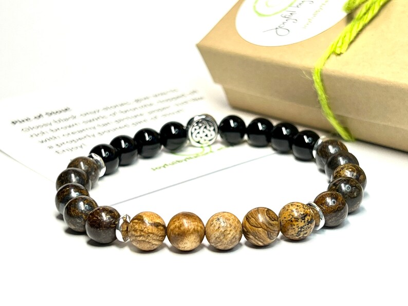 May include: A brown and black beaded bracelet with a silver charm. The bracelet has a Celtic knot design charm and is made with natural stones.