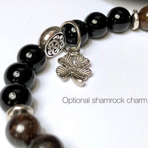 May include: Black and brown beaded bracelet with a silver shamrock charm. The bracelet has a silver bead with a Celtic knot design.