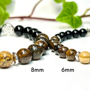 May include: Three bracelets with different sized beads. The top bracelet has black beads and a silver charm. The middle bracelet has brown and black beads. The bottom bracelet has light brown beads. The text "8mm" and "6mm" is printed below the bracelets.