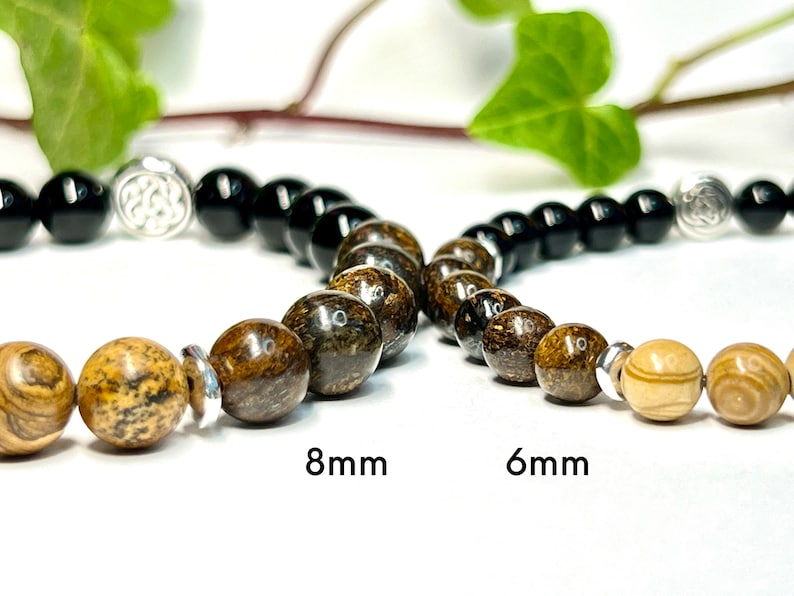 May include: Three bracelets with different sized beads. The top bracelet has black beads and a silver charm. The middle bracelet has brown and black beads. The bottom bracelet has light brown beads. The text "8mm" and "6mm" is printed below the bracelets.