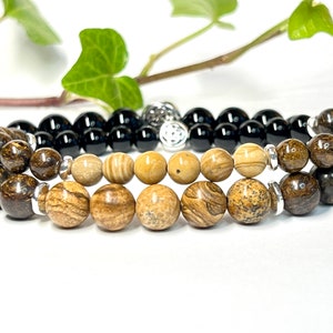 May include: Two bracelets, one with black beads and the other with brown and beige beads. The bracelets are stacked on top of each other.