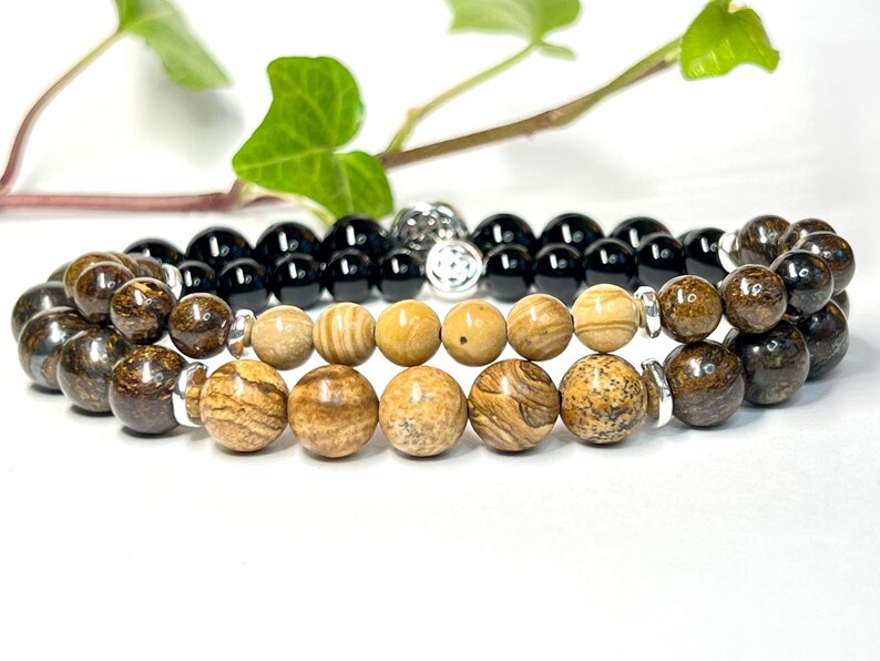 May include: Two bracelets, one with black beads and the other with brown and beige beads. The bracelets are stacked on top of each other.