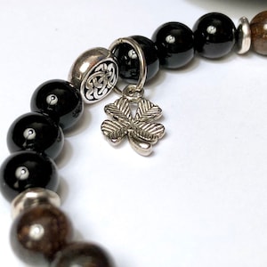May include: Black and brown beaded bracelet with a silver charm in the shape of a four-leaf clover.
