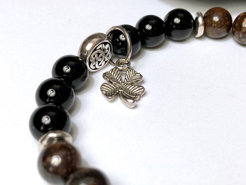 May include: Black and brown beaded bracelet with a silver charm in the shape of a four-leaf clover.