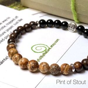 May include: A brown, black, and silver beaded bracelet with a Celtic knot charm. The bracelet is on a white card with the text "Pint of Stout" and a website address.