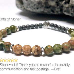 May include: A green and brown stone bracelet with silver accents. The bracelet is made of small, round beads and has a black bead charm. The text "Cliffs of Moher" is visible in the image.