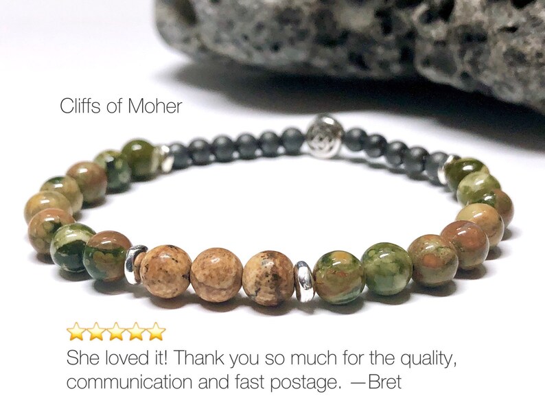 May include: A green and brown stone bracelet with silver accents. The bracelet is made of small, round beads and has a black bead charm. The text "Cliffs of Moher" is visible in the image.