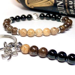 May include: A brown and black beaded bracelet with a silver charm and a matching brown and black beaded keychain with a silver four-leaf clover charm.