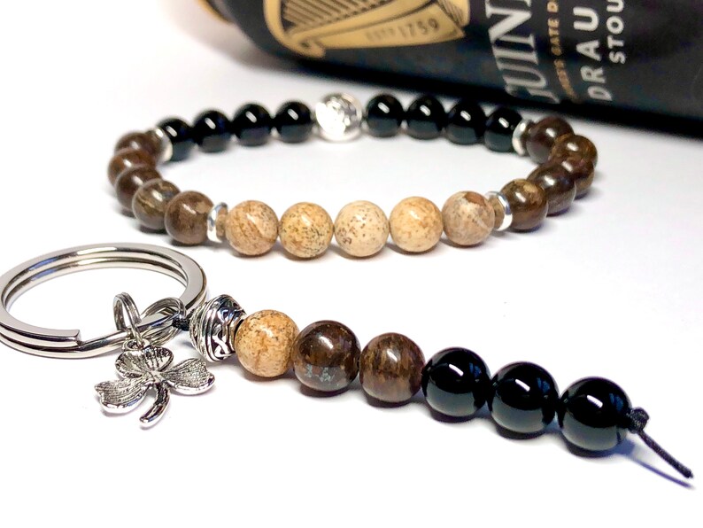 May include: A brown and black beaded bracelet with a silver charm and a matching brown and black beaded keychain with a silver four-leaf clover charm.