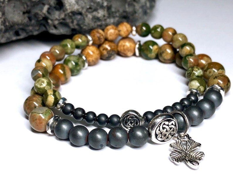 May include: A double-strand bracelet with green, brown, and black beads. The bracelet has a silver Celtic knot charm and a silver shamrock charm.