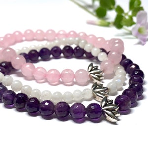 May include: Three layered bracelets with amethyst, moonstone, and rose quartz beads. Each bracelet has a silver lotus flower charm.