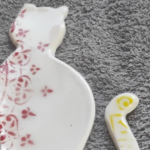Peut inclure: Figurines de chat en céramique blanche avec un motif floral rouge sur le corps et une queue jaune.
