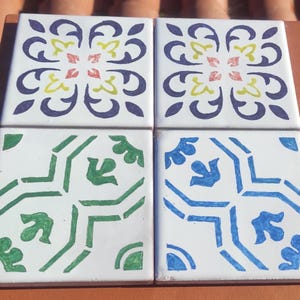 Può includere: Quattro piastrelle in ceramica con diversi motivi geometrici. Le piastrelle sono bianche con disegni blu, verdi, gialli e rossi.