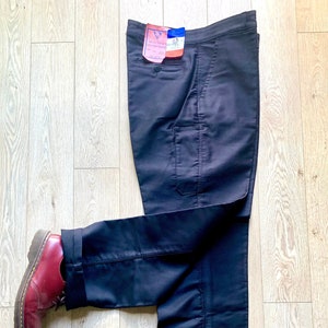 May include: A pair of dark blue cargo pants with a single large pocket on the right leg. The pants are folded and laid on a wooden floor with a pair of red leather shoes on either end.
