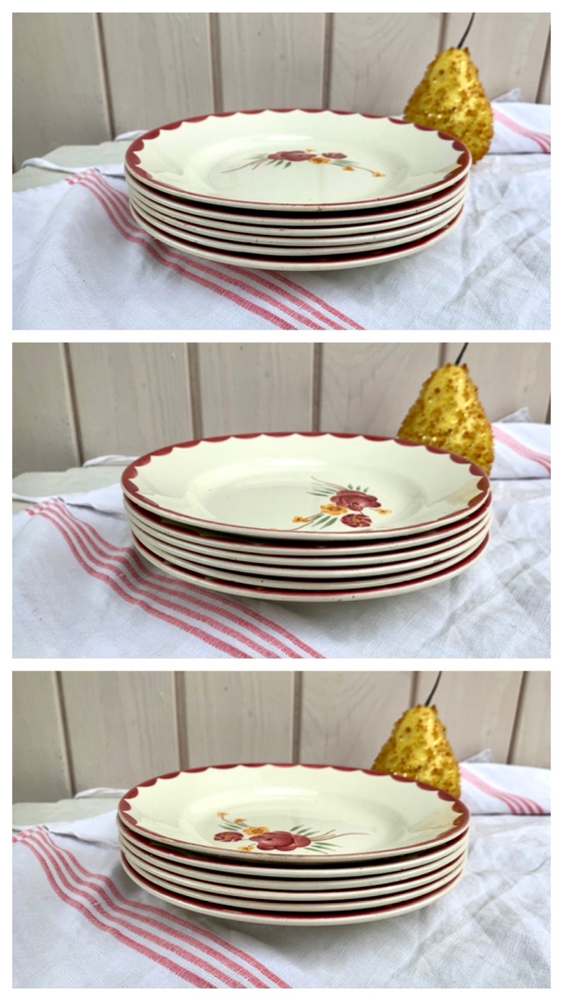 May include: A stack of six white ceramic plates with a red rim and a floral design. The plates are stacked on a white and red striped tablecloth.