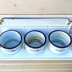 May include: White enamel wall-mounted shelf with three round white enamel containers. The containers have blue trim and are labeled "Savon Mineral", "Savon Noir", and "Cristaux".