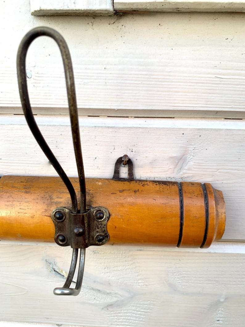 May include: A wooden coat rack with a metal hook. The rack is brown and has a natural wood finish. The hook is silver and has a simple design.