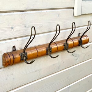 May include: A wooden coat rack with five metal hooks. The rack is made of light brown wood and has a natural finish. The hooks are a dark metal and are in a curved shape.