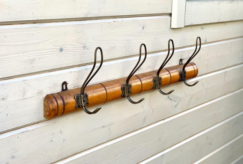 May include: A wooden coat rack with five metal hooks. The rack is made of light brown wood and has a natural finish. The hooks are a dark metal and are in a curved shape.