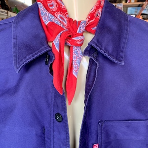 Pode incluir: Uma camisa de trabalho roxa com um bandana paisley vermelho e azul amarrado ao redor do colarinho. A camisa tem um &uacute;nico bolso no lado esquerdo com uma etiqueta vermelha que diz "M".
