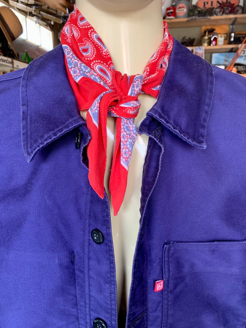 Pode incluir: Uma camisa de trabalho roxa com um bandana paisley vermelho e azul amarrado ao redor do colarinho. A camisa tem um &uacute;nico bolso no lado esquerdo com uma etiqueta vermelha que diz "M".